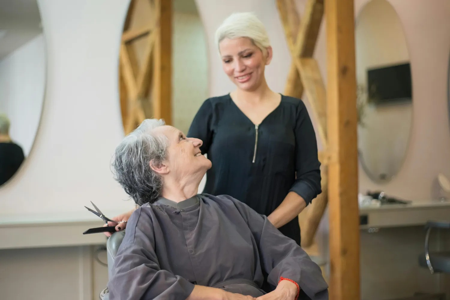 FamilyCare Leipzig UG – Pflegeleistungen für alle Altersgruppen – Dieses Bild zeigt eine ältere Dame, die lächelt, während sie sich in einem Salon die Haare schneiden lässt.